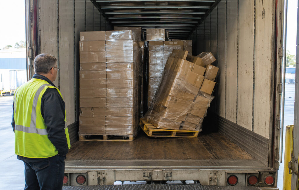 Warehouse worker observing transit damage caused by empty space in the back of a cargo truck.
