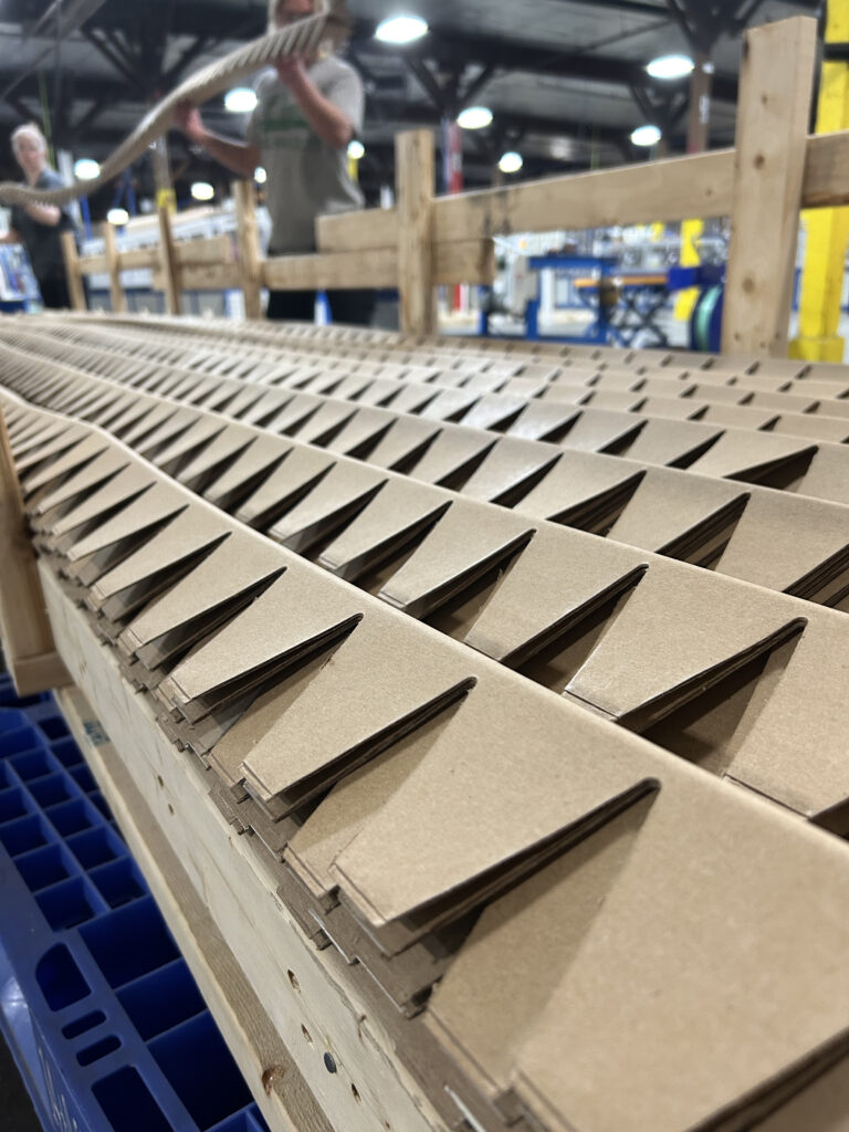 Newly manufactured 18-foot corner board pieces with notches and scoring ready for loading into custom crating skids.